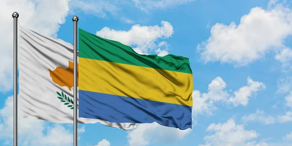 Bandera de Chipre y Gabón ondeando en el viento contra el cielo azul nublado blanco juntos. Concepto diplomático, relaciones internacionales . — Foto de Stock