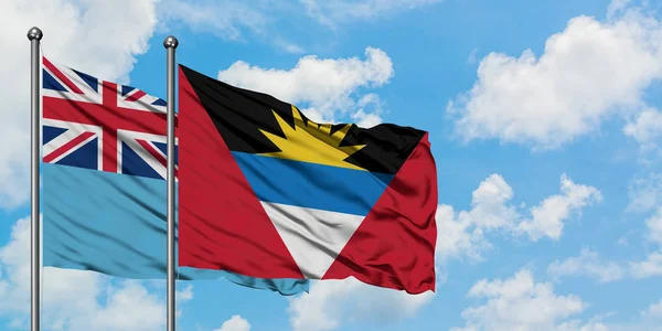 Fiyi y Antigua y Barbuda ondeando en el viento contra el cielo azul nublado blanco juntos. Concepto diplomático, relaciones internacionales . — Foto de Stock