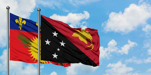 Guadalupe y Papua Nueva Guinea ondeando en el viento contra el cielo azul nublado blanco juntos. Concepto diplomático, relaciones internacionales . — Foto de Stock