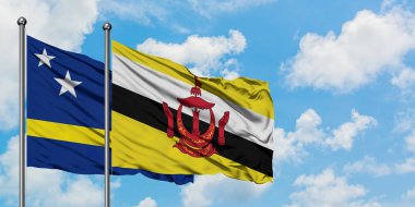 Curacao ve Brunei bayrağı birlikte beyaz bulutlu mavi gökyüzüne karşı rüzgarda sallayarak. Diplomasi kavramı, uluslararası ilişkiler.