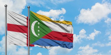 İngiltere ve Komorbayrağı birlikte beyaz bulutlu mavi gökyüzüne karşı rüzgarda sallayarak. Diplomasi kavramı, uluslararası ilişkiler.