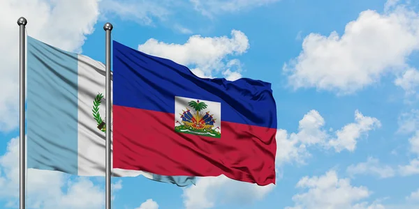 一緒に白い曇った青い空に対して風に手を振るグアテマラとハイチの旗。外交概念、国際関係. — ストック写真