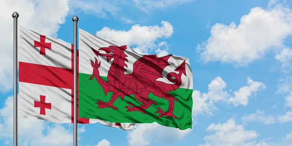 A bandeira da Geórgia e do País de Gales agitando no vento contra o céu azul nublado branco juntos. Conceito de diplomacia, relações internacionais . — Fotografia de Stock