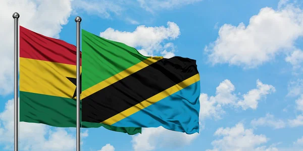 Gana e a bandeira da Tanzânia agitando no vento contra o céu azul nublado branco juntos. Conceito de diplomacia, relações internacionais . — Fotografia de Stock