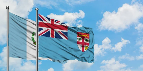 Bandera de Guatemala y Fiyi ondeando en el viento contra el cielo azul nublado blanco juntos. Concepto diplomático, relaciones internacionales . — Foto de Stock