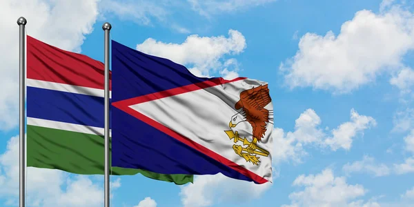 Gambia und die amerikanische Samoa-Flagge wehen gemeinsam im Wind vor dem wolkenverhangenen blauen Himmel. Diplomatie-Konzept, internationale Beziehungen. — Stockfoto