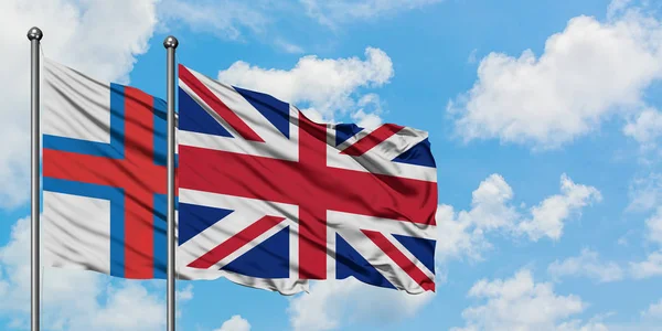 Färöarna och Storbritannien flagga vifta i vinden mot vit grumlig blå himmel tillsammans. Diplomatisk koncept, internationella relationer. — Stockfoto