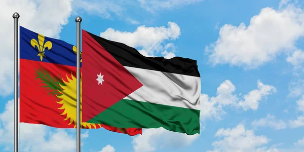 Guadeloupe and Jordan flag waving in the wind against white cloudy blue sky together. Diplomacy concept, international relations.
