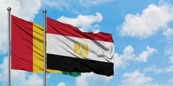 Bandera de Guinea y Egipto ondeando en el viento contra el cielo azul nublado blanco juntos. Concepto diplomático, relaciones internacionales . — Foto de Stock