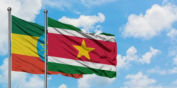 Etiopía y la bandera de Surinam ondeando en el viento contra el cielo azul nublado blanco juntos. Concepto diplomático, relaciones internacionales . — Foto de Stock