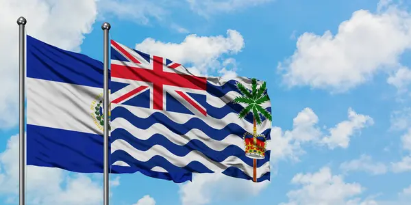Bandera de El Salvador y del Territorio Británico del Océano Índico ondeando en el viento contra el cielo azul nublado blanco juntos. Concepto diplomático, relaciones internacionales . — Foto de Stock