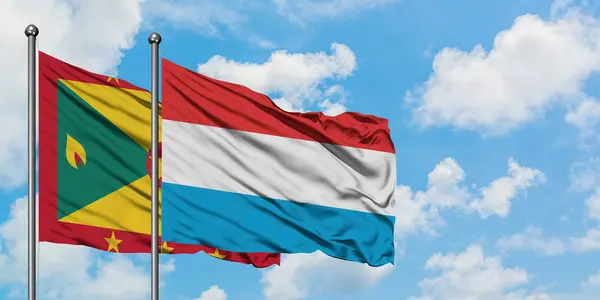 Bandera de Granada y Luxemburgo ondeando en el viento contra el cielo azul nublado blanco juntos. Concepto diplomático, relaciones internacionales . — Foto de Stock
