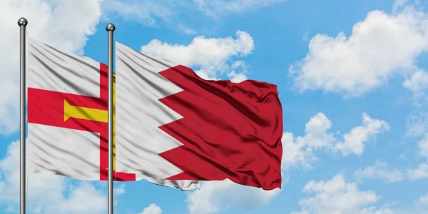 Bandera de Guernsey y Bahréin ondeando en el viento contra el cielo azul nublado blanco juntos. Concepto diplomático, relaciones internacionales . —  Fotos de Stock