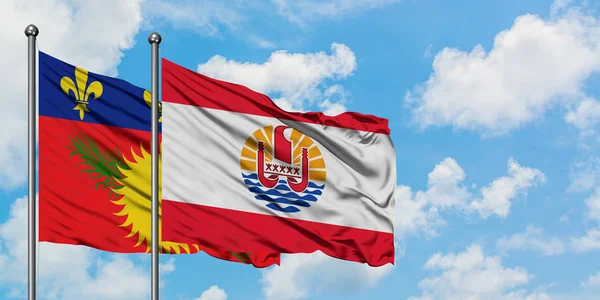 Guadalupe y la bandera de la Polinesia Francesa ondeando en el viento contra el cielo azul nublado blanco juntos. Concepto diplomático, relaciones internacionales . — Foto de Stock