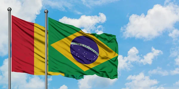 A bandeira da Guiné e do Brasil agitando no vento contra o céu azul nublado branco juntos. Conceito de diplomacia, relações internacionais . — Fotografia de Stock