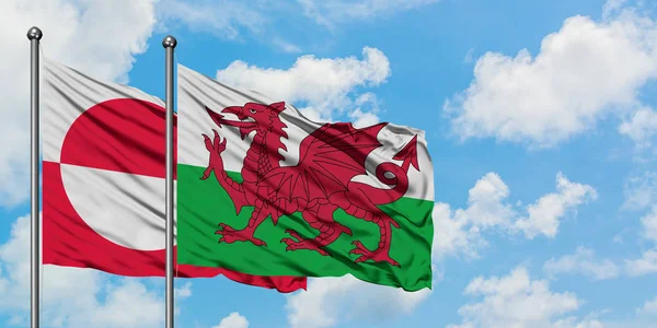 Bandeira da Groenlândia e País de Gales agitando no vento contra o céu azul nublado branco juntos. Conceito de diplomacia, relações internacionais . — Fotografia de Stock