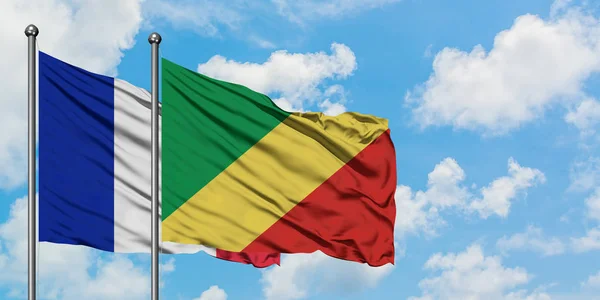 Frankreich und die Republik Kongo wehen gemeinsam im Wind vor dem wolkenverhangenen blauen Himmel. Diplomatie-Konzept, internationale Beziehungen. — Stockfoto