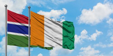 Gambiya ve Fildişi Sahili bayrağı birlikte beyaz bulutlu mavi gökyüzüne karşı rüzgarda sallayarak. Diplomasi kavramı, uluslararası ilişkiler.