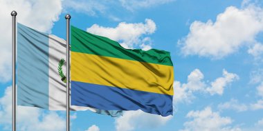 Guatemala ve Gabon bayrağı birlikte beyaz bulutlu mavi gökyüzüne karşı rüzgarda sallayarak. Diplomasi kavramı, uluslararası ilişkiler.