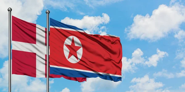 Danimarka ve Kuzey Kore bayrağı birlikte beyaz bulutlu mavi gökyüzüne karşı rüzgarsal sallayarak. Diplomasi kavramı, uluslararası ilişkiler. — Stok fotoğraf