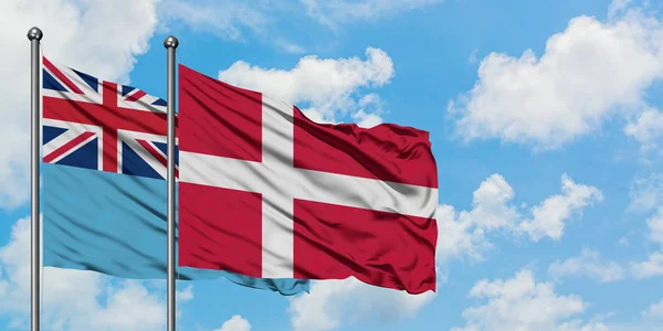 Fidži a Dánsko vlaje ve větru proti bíle zatažené modré obloze. Diplomacie, mezinárodní vztahy. — Stock fotografie
