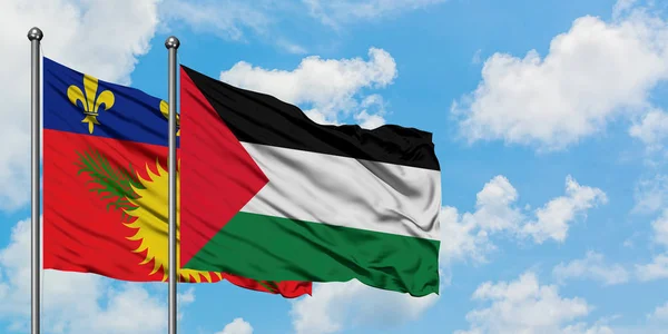 Guadalupe y la bandera de Palestina ondeando en el viento contra el cielo azul nublado blanco juntos. Concepto diplomático, relaciones internacionales . — Foto de Stock