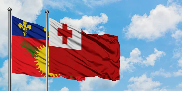 Guadalupe y la bandera de Tonga ondeando en el viento contra el cielo azul nublado blanco juntos. Concepto diplomático, relaciones internacionales . —  Fotos de Stock