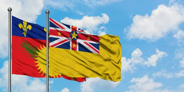 Guadalupe y la bandera de Niue ondeando en el viento contra el cielo azul nublado blanco juntos. Concepto diplomático, relaciones internacionales . — Foto de Stock