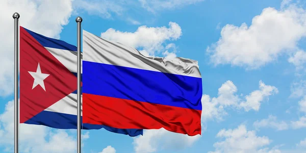 Kuba- und Russland-Flagge wehen gemeinsam im Wind gegen den wolkenverhangenen blauen Himmel. Diplomatie-Konzept, internationale Beziehungen. — Stockfoto