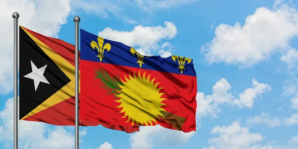 Timor Oriental y Guadalupe ondeando en el viento contra el cielo azul nublado blanco juntos. Concepto diplomático, relaciones internacionales . — Foto de Stock