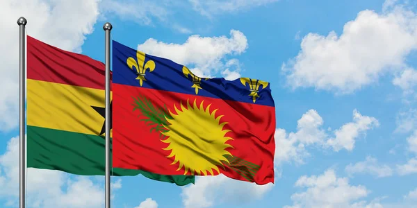 Bandera de Ghana y Guadalupe ondeando en el viento contra el cielo azul nublado blanco juntos. Concepto diplomático, relaciones internacionales . — Foto de Stock