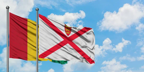Bandera de Guinea y Jersey ondeando en el viento contra el cielo azul nublado blanco juntos. Concepto diplomático, relaciones internacionales . — Foto de Stock