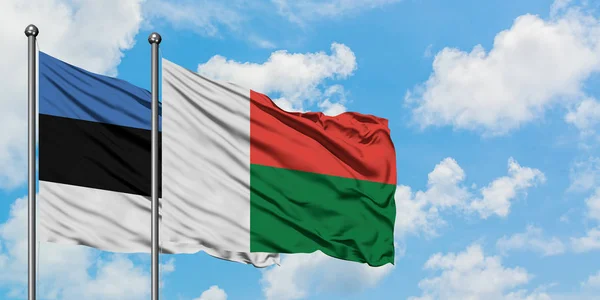 Bandera de Estonia y Madagascar ondeando en el viento contra el cielo azul nublado blanco juntos. Concepto diplomático, relaciones internacionales . — Foto de Stock