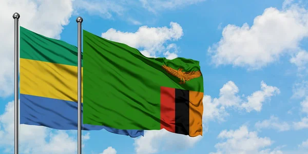 Gabão e Zâmbia acenando com o vento contra o céu azul nublado branco juntos. Conceito de diplomacia, relações internacionais . — Fotografia de Stock