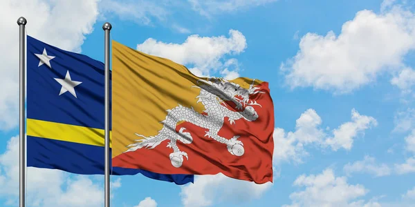 Κουρασάο και Μπουτάν σημαία κουνώντας τον άνεμο ενάντια λευκό συννεφιασμένο γαλάζιο του ουρανού μαζί. Φιλοσοφία της διπλωματίας, διεθνείς σχέσεις. — Φωτογραφία Αρχείου