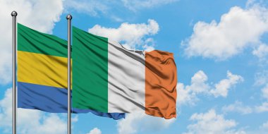 Gabon ve İrlanda bayrağı birlikte beyaz bulutlu mavi gökyüzüne karşı rüzgarda sallayarak. Diplomasi kavramı, uluslararası ilişkiler.