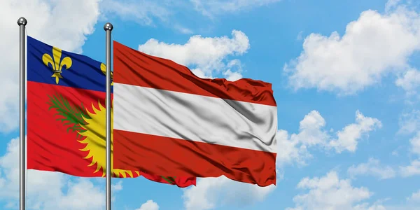 Guadalupe y Austria bandera ondeando en el viento contra el cielo azul nublado blanco juntos. Concepto diplomático, relaciones internacionales . — Foto de Stock