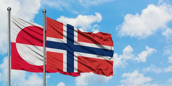 Gemeinsam wehen grönländische und norwegische Flaggen im Wind gegen den wolkenverhangenen blauen Himmel. Diplomatie-Konzept, internationale Beziehungen. — Stockfoto