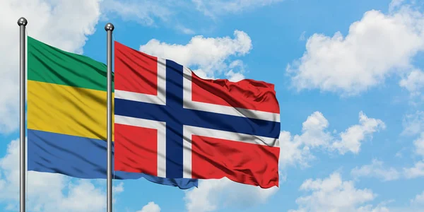 Bandera de Gabón y Bouvet Islands ondeando en el viento contra el cielo azul nublado blanco juntos. Concepto diplomático, relaciones internacionales . — Foto de Stock