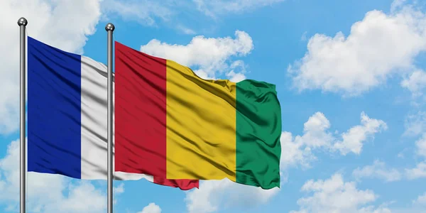 A bandeira da França e da Guiné agitando no vento contra o céu azul nublado branco juntos. Conceito de diplomacia, relações internacionais . — Fotografia de Stock