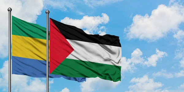 Gabón y la bandera de Palestina ondeando en el viento contra el cielo azul nublado blanco juntos. Concepto diplomático, relaciones internacionales . — Foto de Stock