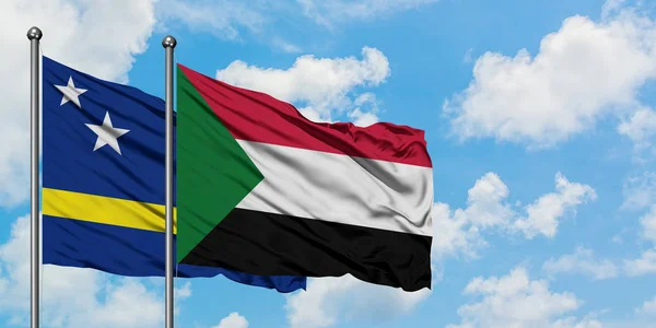 Bandera de Curazao y Sudán ondeando en el viento contra el cielo azul nublado blanco juntos. Concepto diplomático, relaciones internacionales . — Foto de Stock