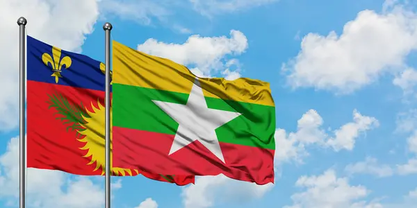 Guadalupe y la bandera de Myanmar ondeando en el viento contra el cielo azul nublado blanco juntos. Concepto diplomático, relaciones internacionales . — Foto de Stock