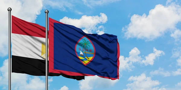 Bandera de Egipto y Guam ondeando en el viento contra el cielo azul nublado blanco juntos. Concepto diplomático, relaciones internacionales . — Foto de Stock
