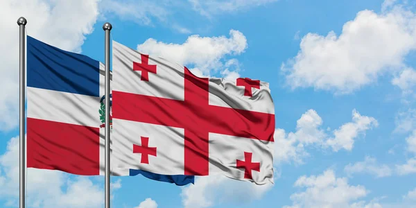 Bandera de República Dominicana y Georgia ondeando en el viento contra el cielo azul nublado blanco juntos. Concepto diplomático, relaciones internacionales . — Foto de Stock