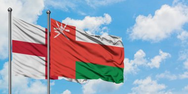 İngiltere ve Umman bayrağı birlikte beyaz bulutlu mavi gökyüzüne karşı rüzgarda sallayarak. Diplomasi kavramı, uluslararası ilişkiler.