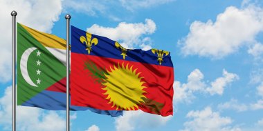 Komorlar ve Guadeloupe bayrağı birlikte beyaz bulutlu mavi gökyüzüne karşı rüzgarda sallayarak. Diplomasi kavramı, uluslararası ilişkiler.