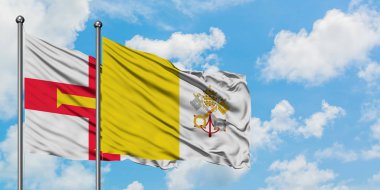 Guernsey ve Vatikan bayrağı birlikte beyaz bulutlu mavi gökyüzüne karşı rüzgarda sallayarak. Diplomasi kavramı, uluslararası ilişkiler.