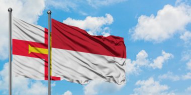 Guernsey ve Endonezya bayrağı birlikte beyaz bulutlu mavi gökyüzüne karşı rüzgarda sallayarak. Diplomasi kavramı, uluslararası ilişkiler.