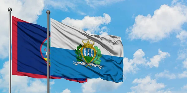 Guam och San Marino sjunker vifta i vinden mot vit grumlig blå himmel tillsammans. Diplomatisk koncept, internationella relationer. — Stockfoto